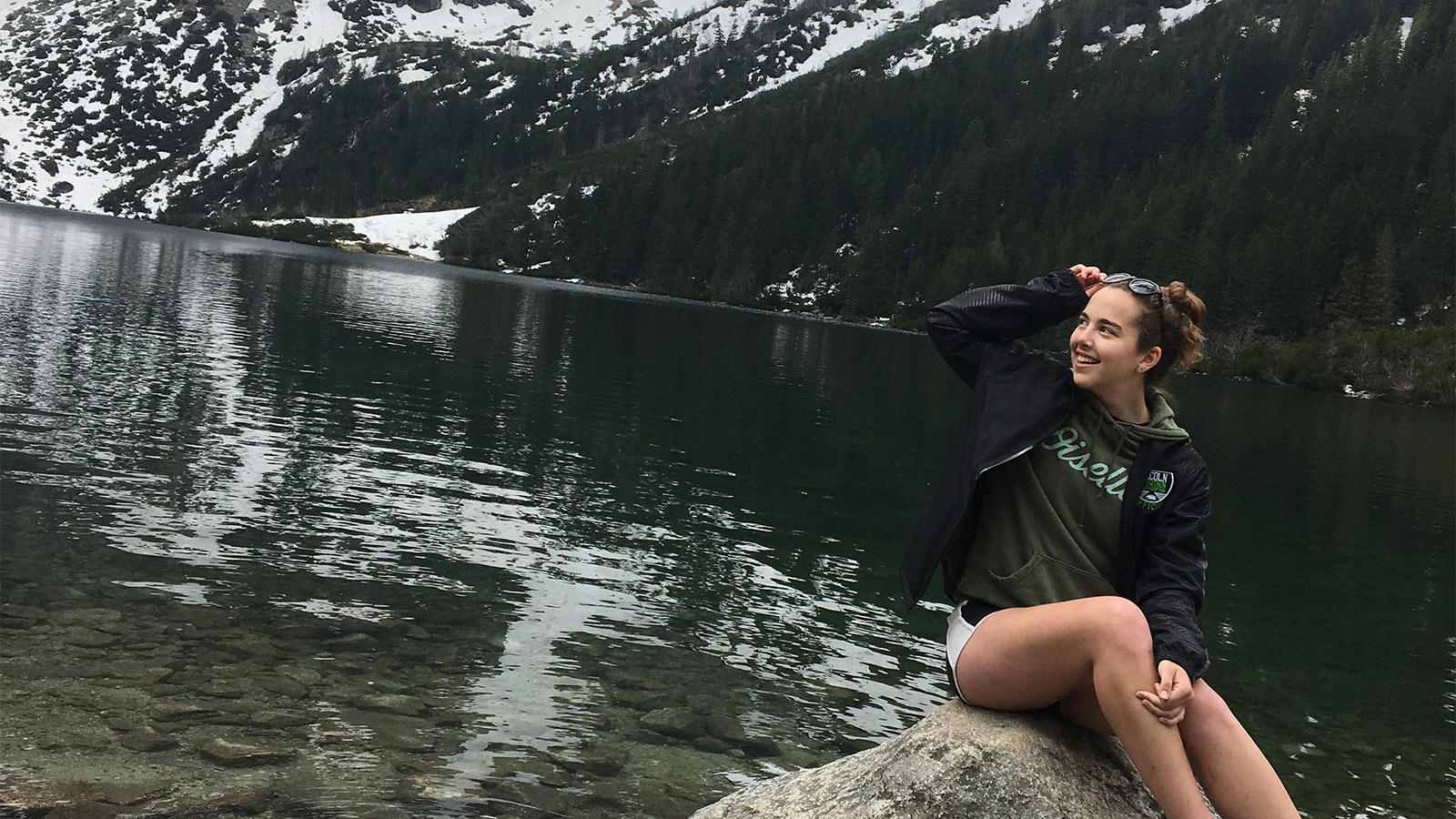 student sitting on rock by lake