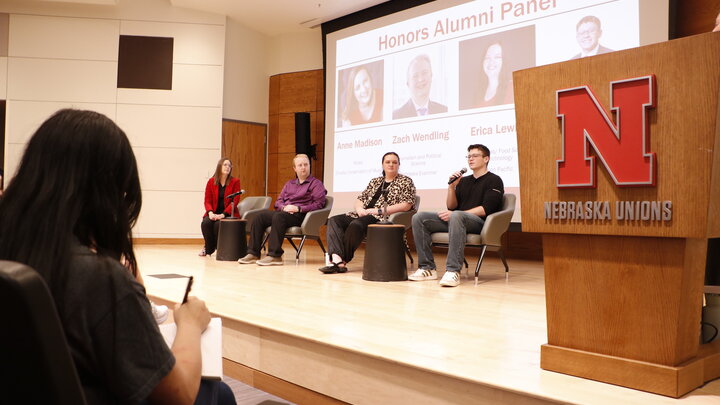 Four panelists seated on stage for an Honors Alumni Panel in a Nebraska Unions auditorium.