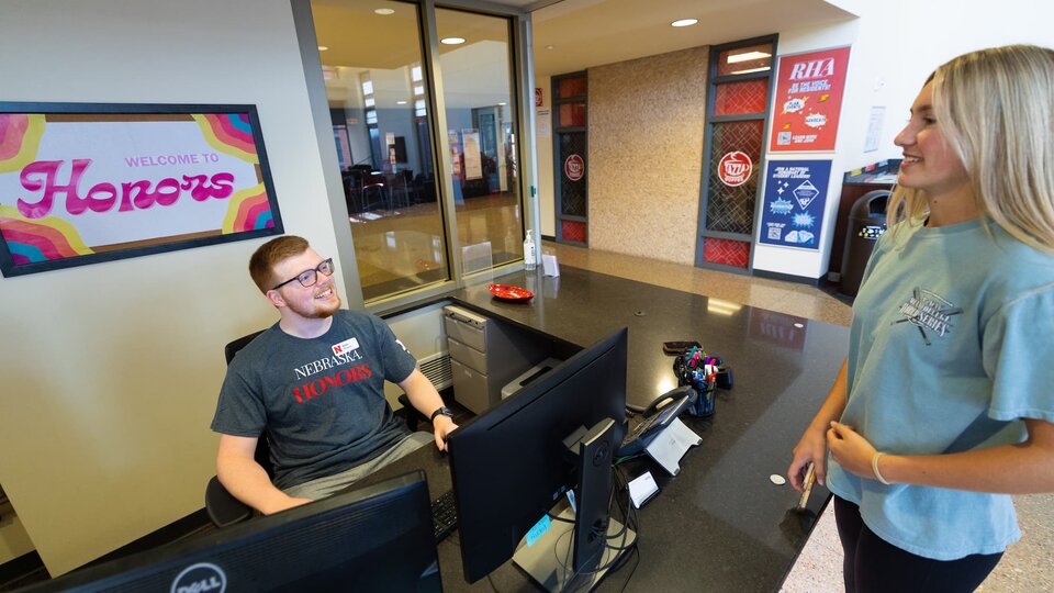 Student at a reception desk with "Welcome to Honors" sign on the wall.