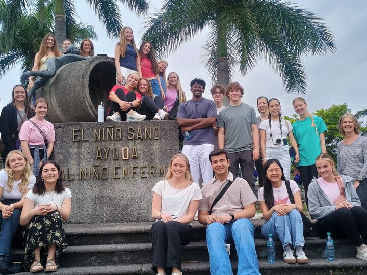 Group of people smiling near a stone monument surrounded by palm trees.