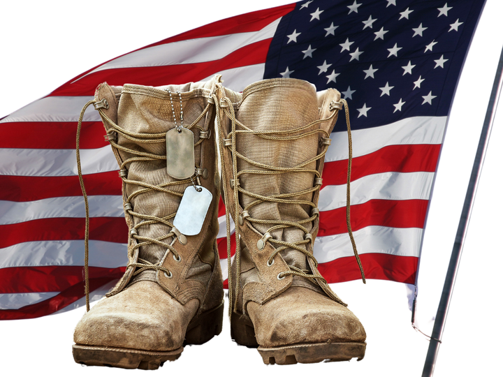 solider boots with dog tags hanging on them; american flag in the background