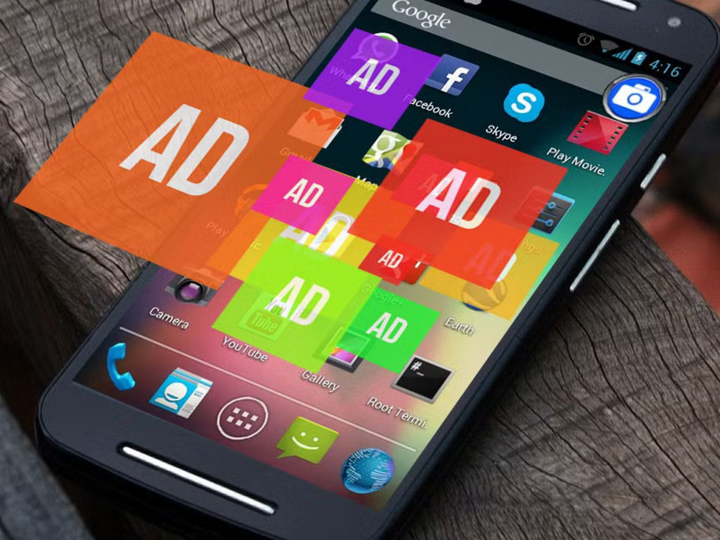 Smartphone screen filled with colorful ad banners, resting on a wooden surface.