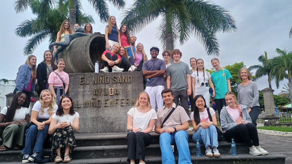 Group of people smiling near a stone monument surrounded by palm trees.